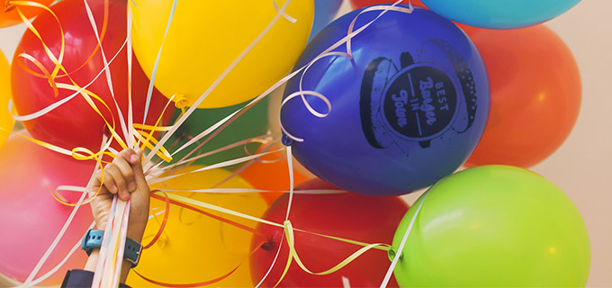 Mehrere bunte Luftballons sind mit einem Logo bedruckt.
